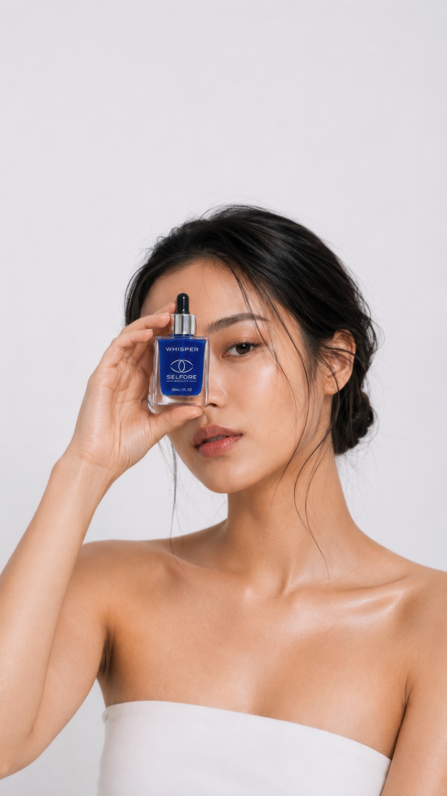 A woman holding the Whisper bottle over one eye, glowing skin, soft studio light